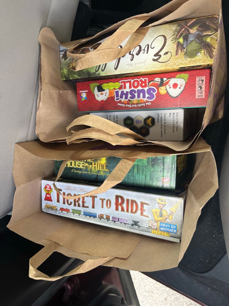 Two brown paper bags containing board games I received for free. They are ticket to ride, betrayal at house on the hill, hive, sushi roll and everdell. 