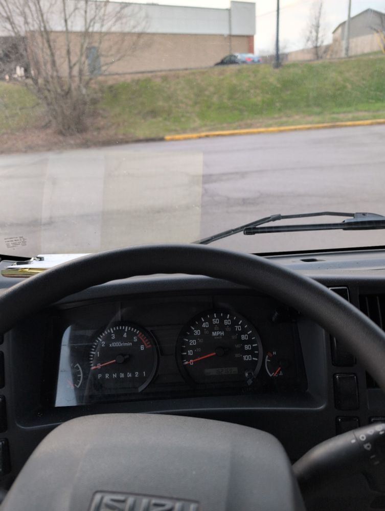 View of the steering wheel of an Isuzu vehicle, looking at the side of a hill, along with the side of a building
