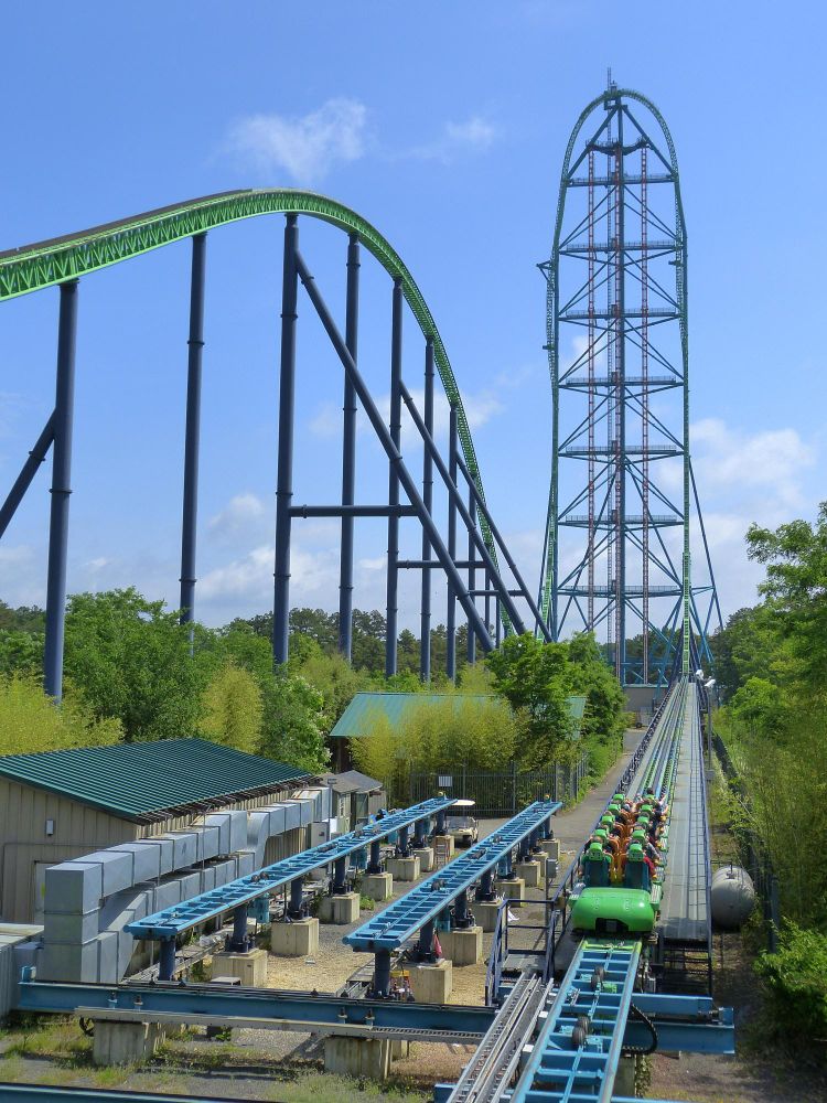 Von Gemini: 

Ein hochauflösendes, mittleres Foto zeigt die riesige grüne und blaue Achterbahn „Kingda Ka“ mit einem vertikalen Anstieg und einer horizontalen, geschwungenen Strecke, die von hohen, dunkelblauen Stützen getragen wird. Die Strecke verläuft von rechts nach links und biegt dann nach oben und über den Horizont ab, während die vertikale Aufwärtsstrecke der Achterbahn nach rechts hin steil nach oben abfällt. Die grüne Schiene der Achterbahn ist unten in der Bildmitte zu sehen, wo ein grüner Zug mit Fahrgästen auf dem Weg nach oben ist. Die Landschaft ist sonnig, mit bewölktem Himmel und üppig grünen Bäumen an der Unterseite des Rahmens.
