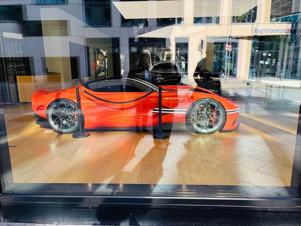 Orangefarbener Sportwagen in einem Schaufenster. Die Umgebung spiegelt sich im Glas.