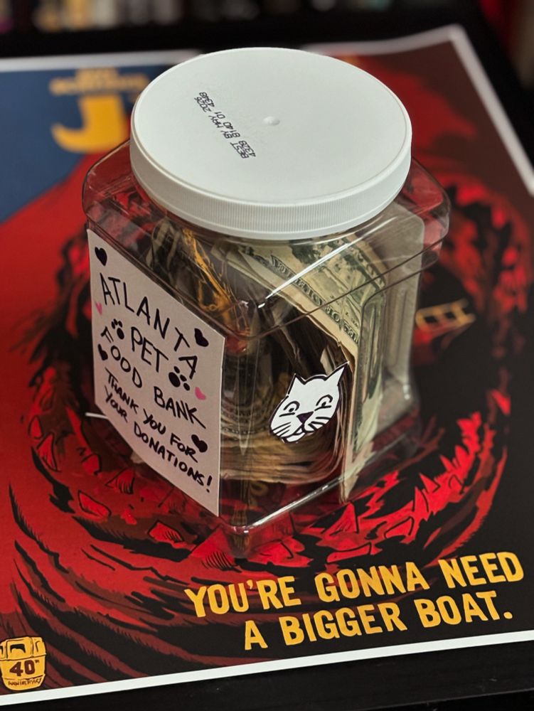 A photo of a cat food container filled with cash. A label on the front says “Atlanta pet food bank - thank you for your donations”