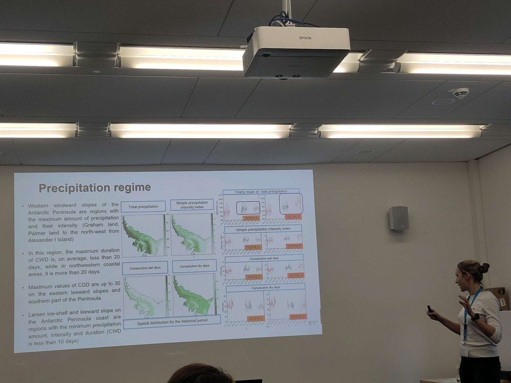 Woman stands next to a screen showing a slide with maps of the Antarctic peninsula and summary of results