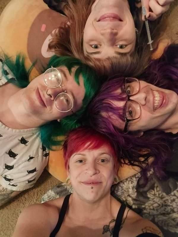 4 friends laying on the floor with their heads poking from off screen on each side. A syringe is being held by one person. 