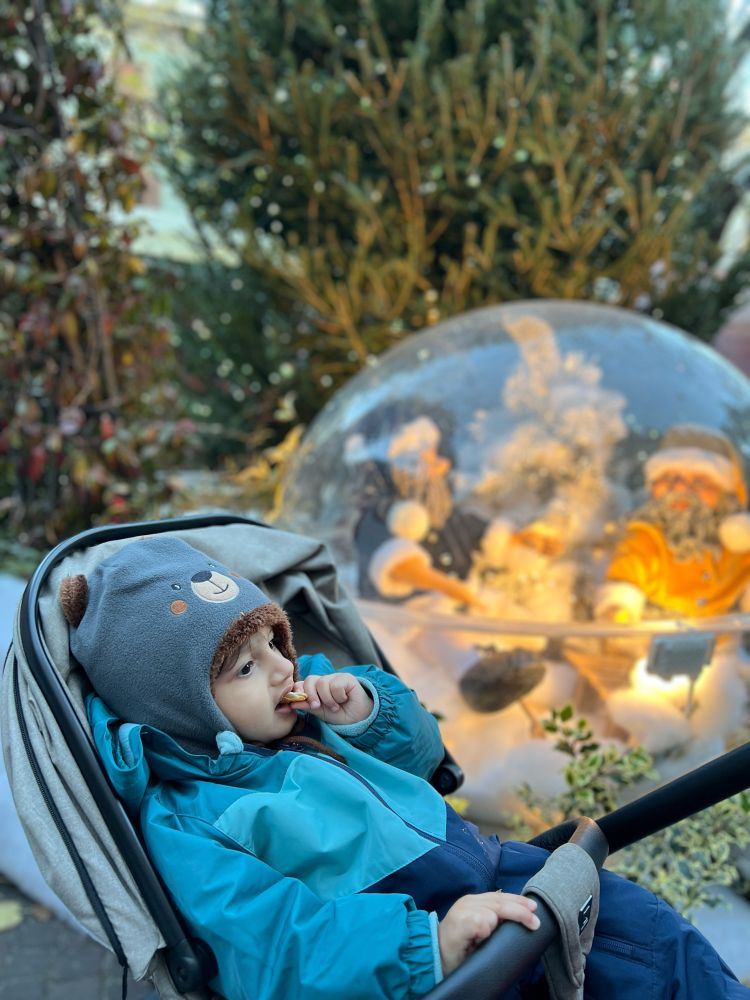 My son yahya in verona Christmas market with Christmas decorations in background, eating a biscuit in his stroller wearing a cute cap