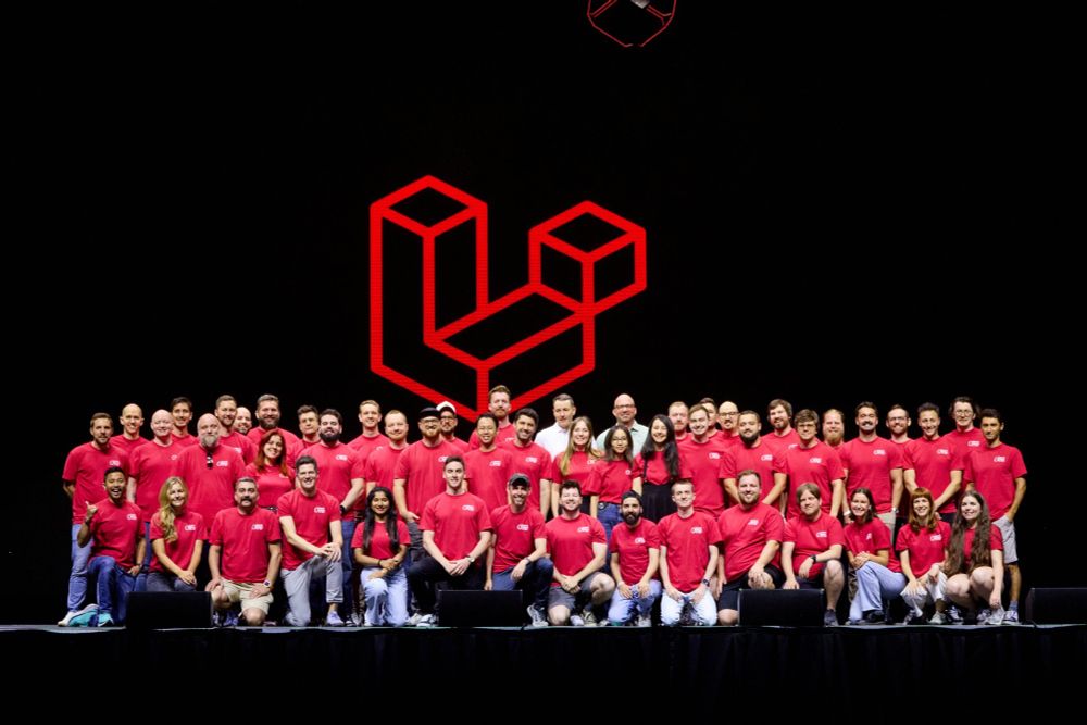 A group photo of the Laravel team wearing red shirts and posing on the stage smiling.