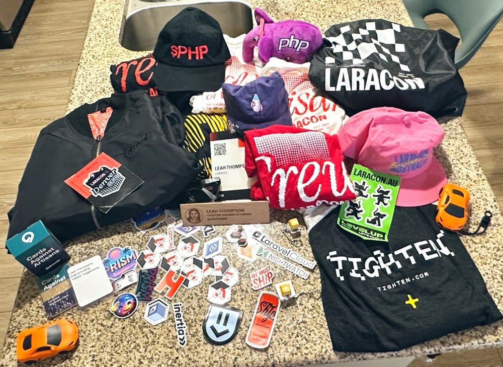 A ton of merch and swag from Laracon that includes stuff from Laravel and other companies like Sentry and Tighten. The merch is spread out on a granite countertop.