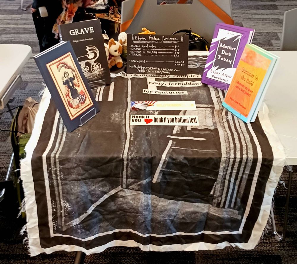 Books Train, Grave, Mother Died Today, and Summer in the Field around Honk of you <3 Honk if you bottom text and sellyourbones.com bumper stickers on top of a printed tapestry of collage poetry all made by Edgar. Bonus SnipSnip, a two headed beanie baby cat made by Birde peeking behind the books.