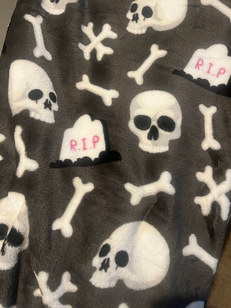 A grey plush blanket with white skulls and bones and white tombstones with pink letters on them that say R.I.P