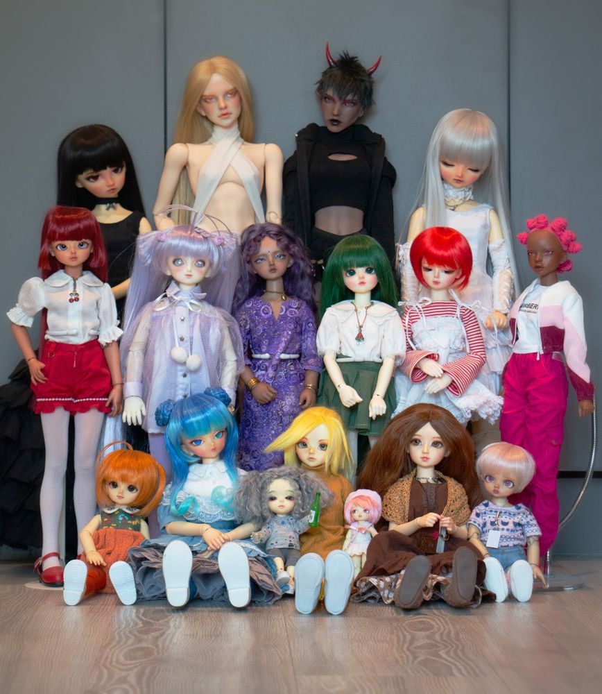 A group of 17 colourful ball-jointed dolls of various sizes are posed together