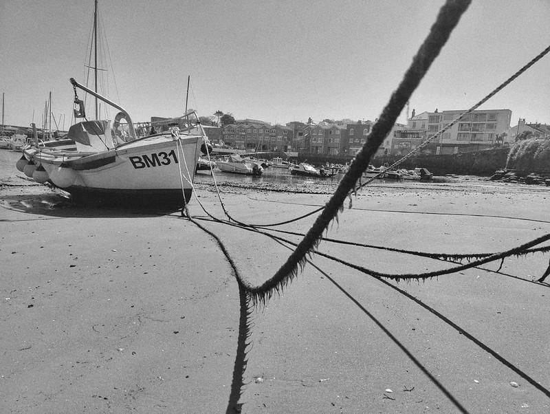 A monochrome (B & W) version ... A seaweed draped rope stretched over a sandy edge of Paignton Harbour, tethering a small fishing vessel.
