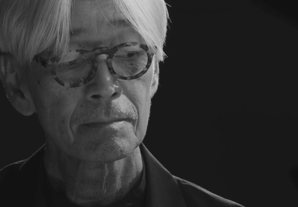 Close frame of Ryuichi Sakamoto's face while he is playing.   