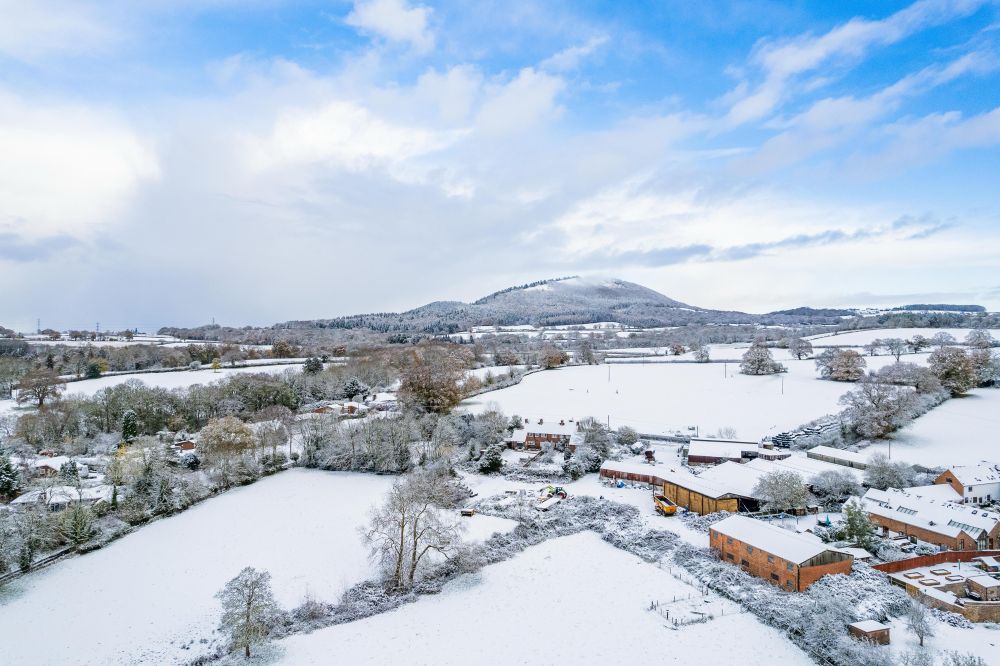 A picture taken using a drone showing farmland building s and the wrekin covered in snow 
