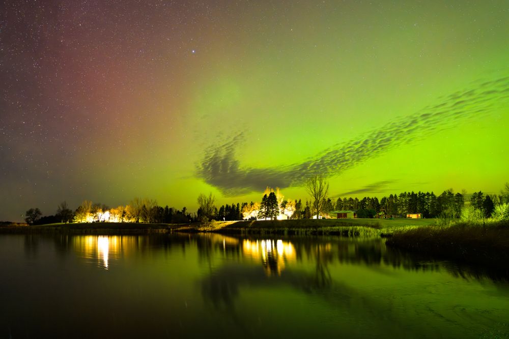 The Northern Lights shine over a lake. The sky is mainly green, with some red appearing in the upper left side. A cloud makes the appearance of the Nike Swoosh logo, appearing as a dark gray logo in front of bright green sky.

The water is perfectly still, reflecting the sky and the campground lights on the far side of the lake from the photographer.