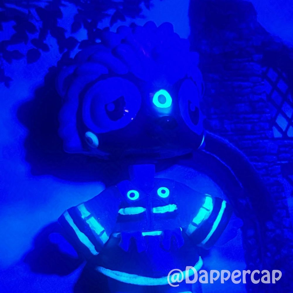 A closeup blacklight picture of a hand-painted hybrid mini doll inspired by Silver the Hedgehog, floating in some overgrown ruins.

Head came from a Littlest Pet Shop Hedgehog and the body/outfit came from a Yummiland Doll.