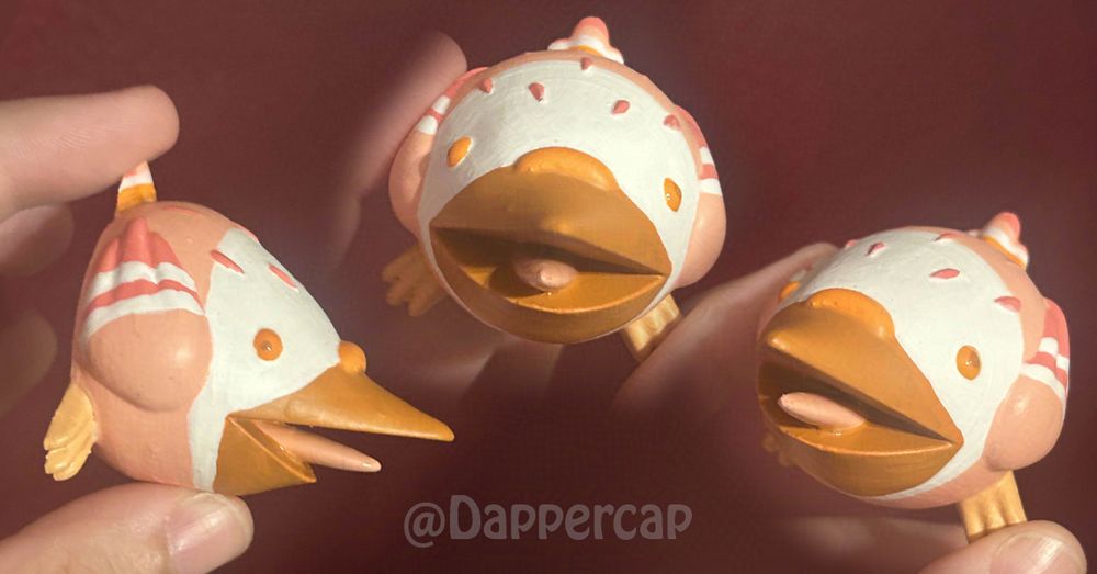 A small stylized figurine of a pigeon screaming. Its color scheme is borrowed from the Lesbian Pride Flag, with a white and light pink body, pinker feathers and wing tips, bright orange eyes and feet, and a dark orange beak.