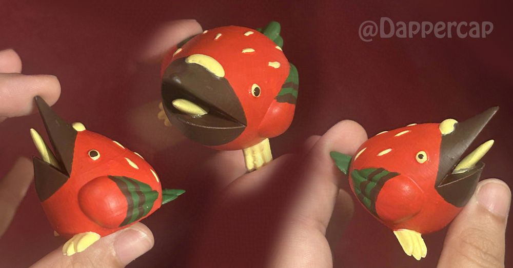 A small stylized figurine of a screaming pigeon. It's color scheme is reminiscent of a strawberry, with a bright red body, seed like feathers, a dark brown beak, and green feathers on its tail and wing tips.