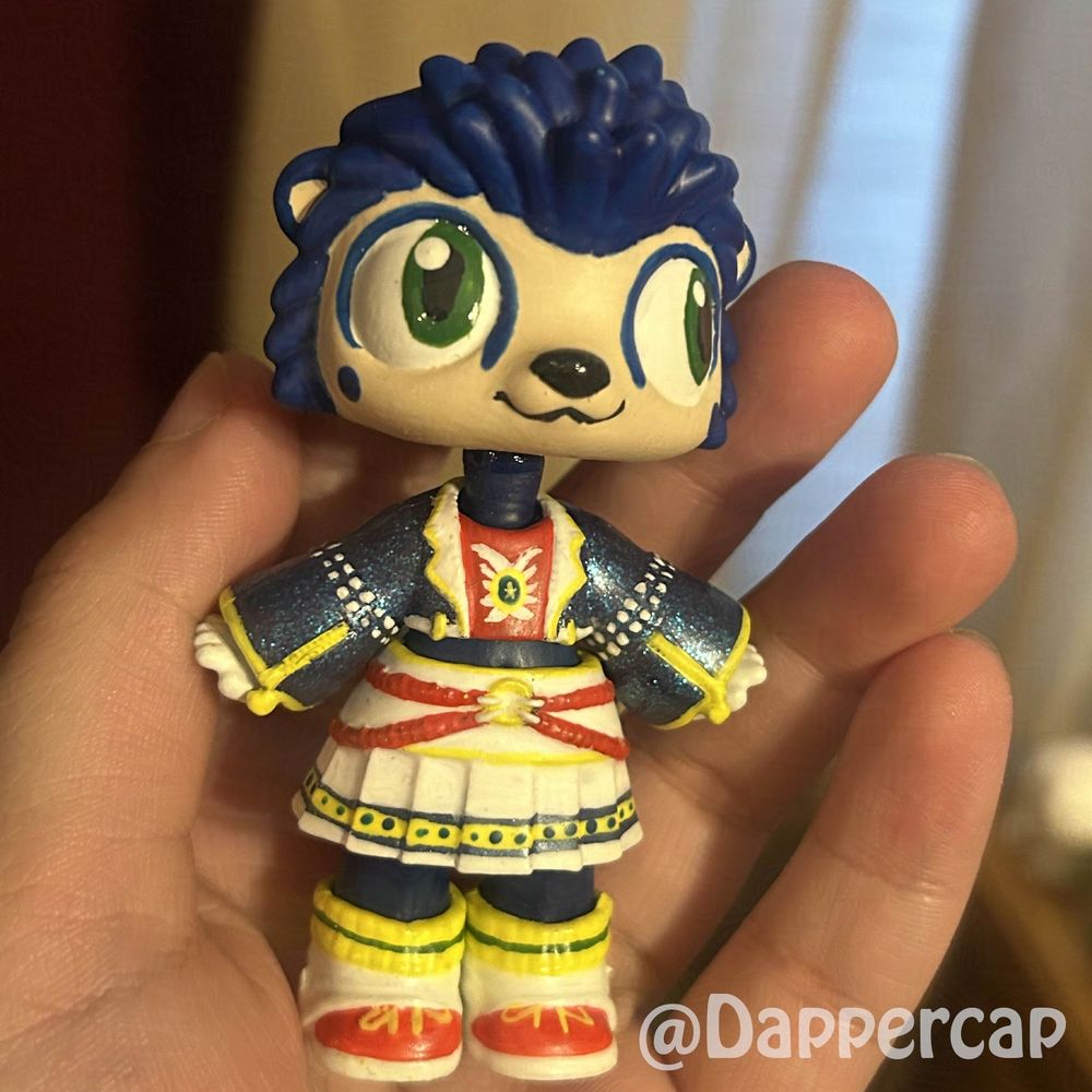 A handprinted custom hybrid mini doll inspired by Sonic the Hedgehog, standing in the green hill zone, surrounded by little golden rings. 

Head came from a Littlest Pet Shop Hedgehog and the outfit/body came from a Yummiland keychain doll.