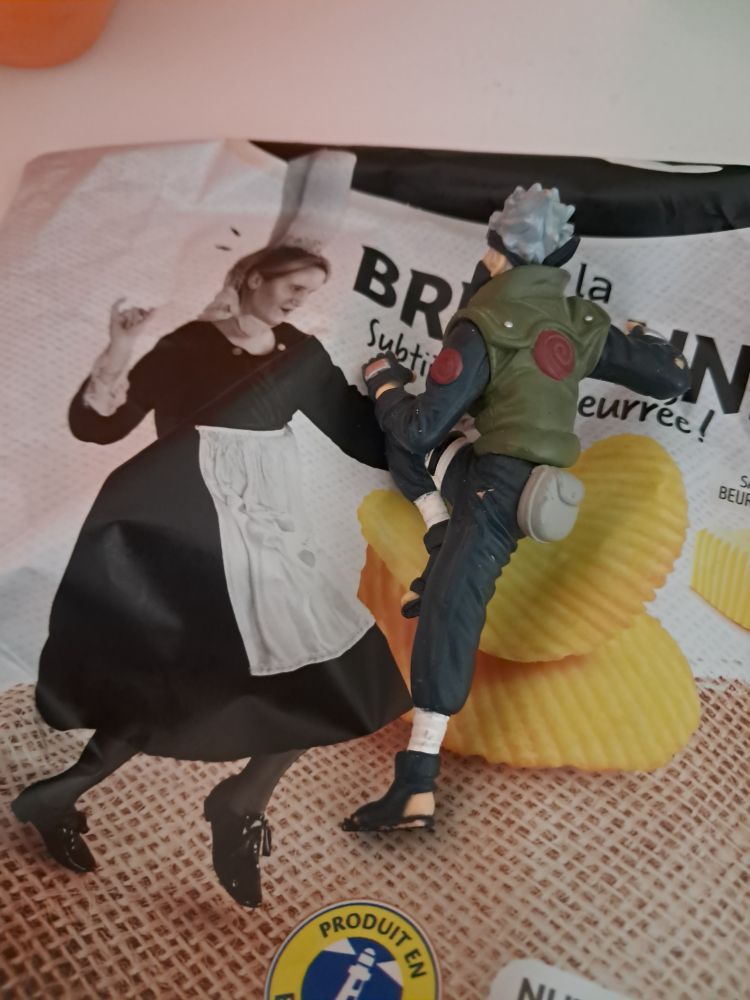 Photo d'une figurine de Kakashi posée sur un paquet de chips donnant l'illusion d'une danse endiablée avec la danseuse bretonne du paquet. 
Joli !