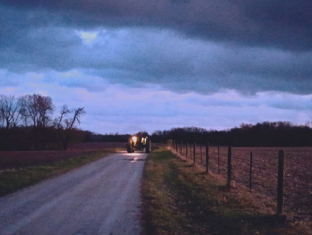 Tractor driving away down a gravel driveway under heavy clouds.