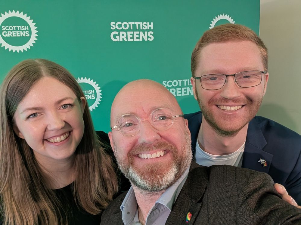Patrick Harvie in a selfie with Gillian Mackay and Ross Greer, with Scottish Green Party logos on the backdrop