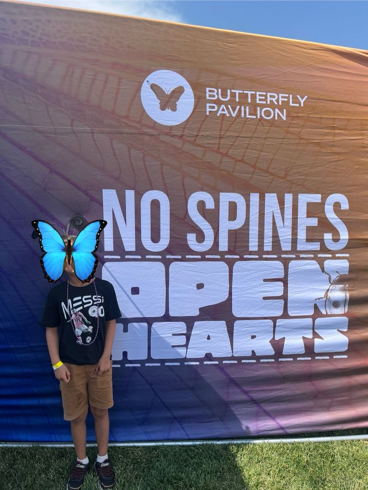 Photo of a child standing in front of a sign saying “Butterfly Pavillion No Spines Open Hearts”