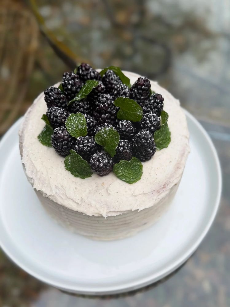 A blackberry pistachio cake decorated with fresh blackberries and mint leaves 