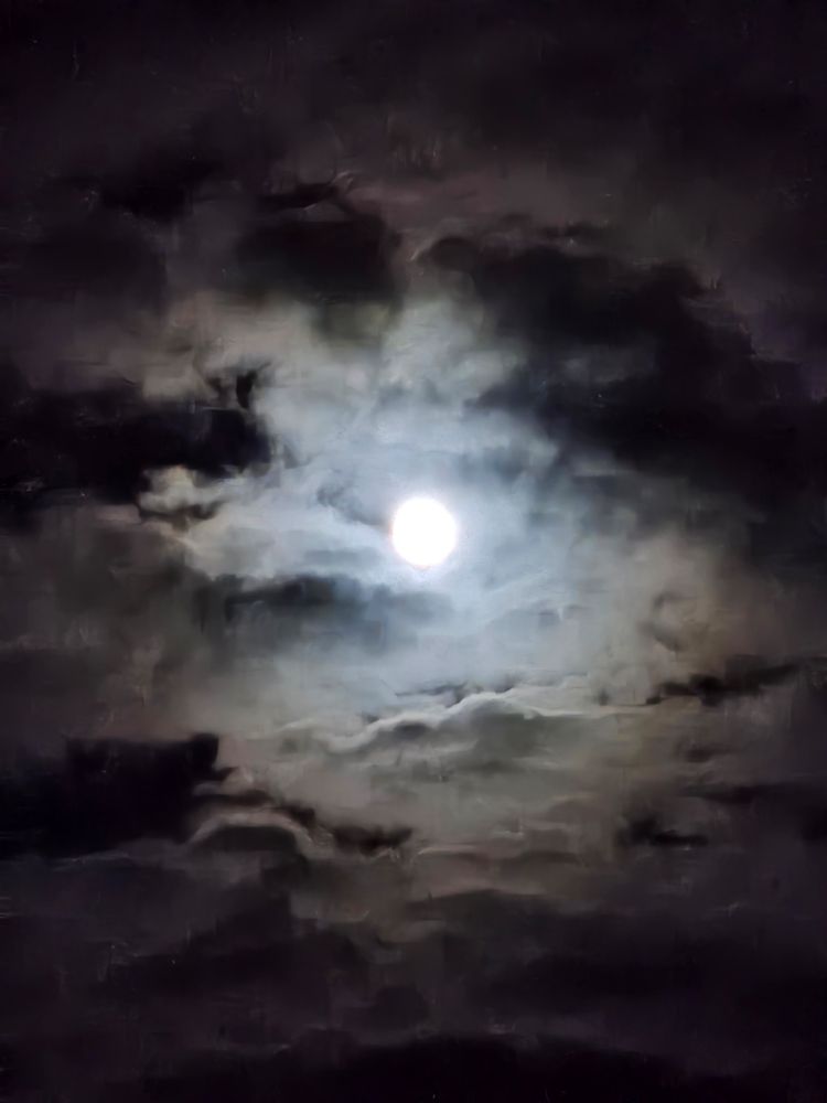 Der fast volle Mond hinter lückenhaft Wolken. Durch die Atmosphäre sieht man um den Mond einen Halo, innen hell weiß und am Rand leicht rötlich.