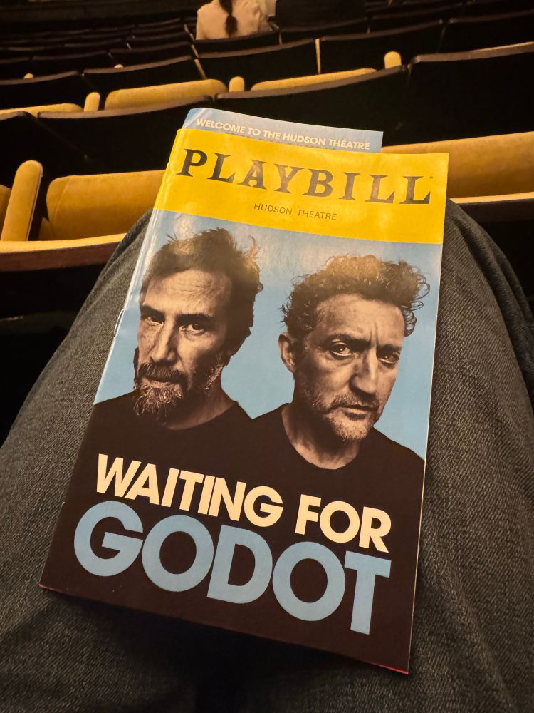 A playbill for Waiting for Godot, starring Keanu Reeves and Alex Winters, sits on a lap.