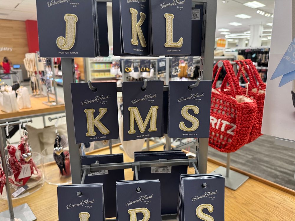 Iron on patches appear on a display stand in a retail store. The letters K M and S are put next to each other in a row.