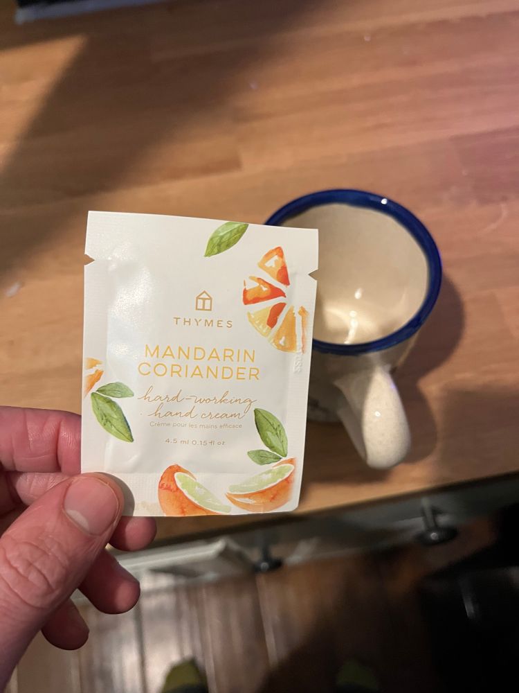 a packet of mandarin coriander hand cream poised above a tea cup