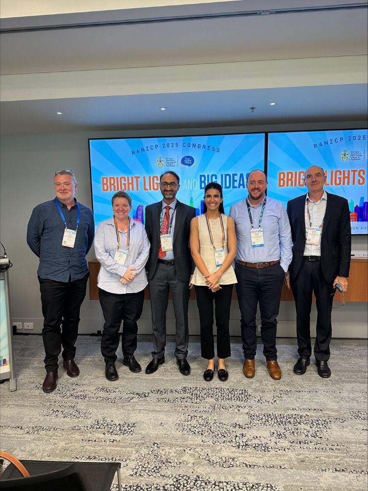 Symposium co-presenters in front of large screens reading "Bright Lights Big Ideas".  People in the photo are: 
Daniel Houghton
Irene Clelland
Neeraj Gill
Jappan Sawhney
Andrew Wilson
Stefan Preissler 
