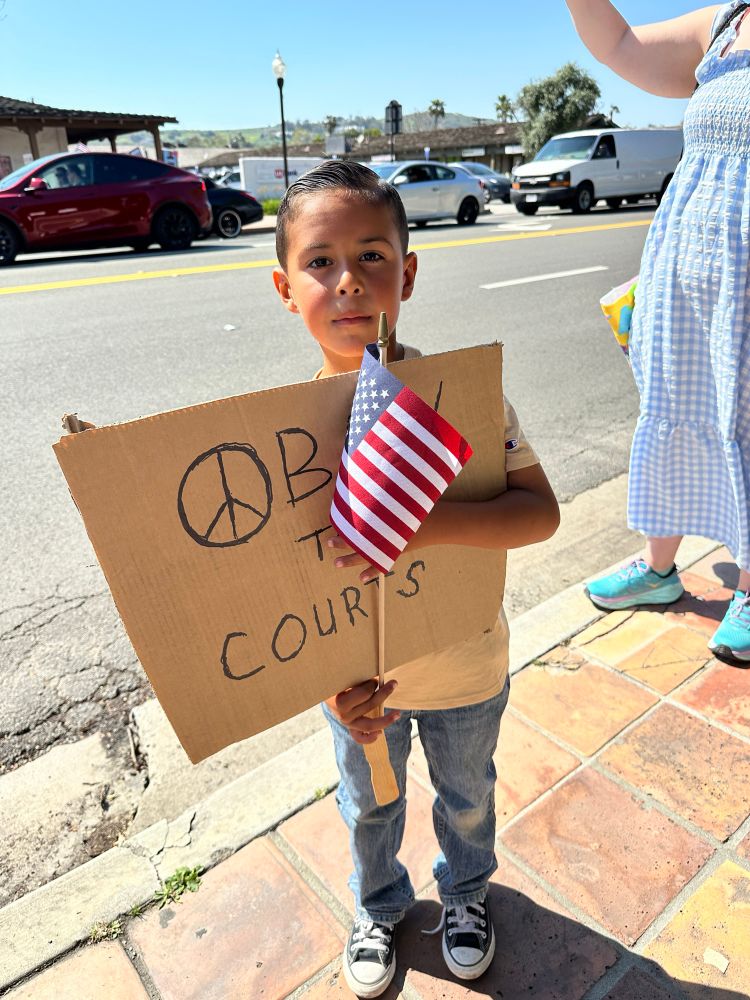 This boy is holding a protest sign that reads “Obey the Courts”