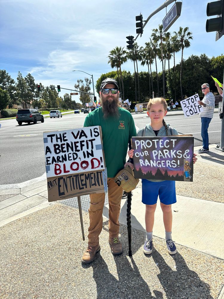 Two protestors standing on a street corner in Irvine CA with signs that read: protect our Parks and Rangers

The VA is a benefit earned in blood not entitlement 