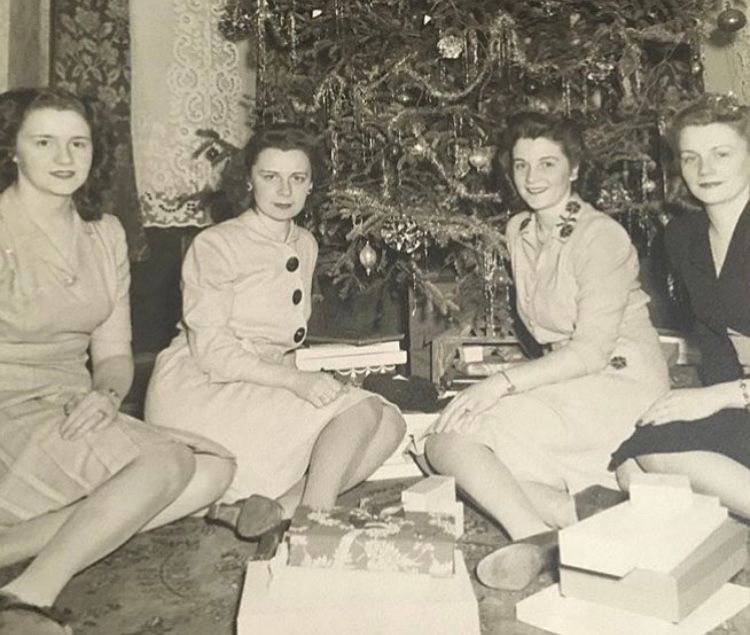 four girls in the 1940s sit in front of a large decorated christmas tree. photo is black and white