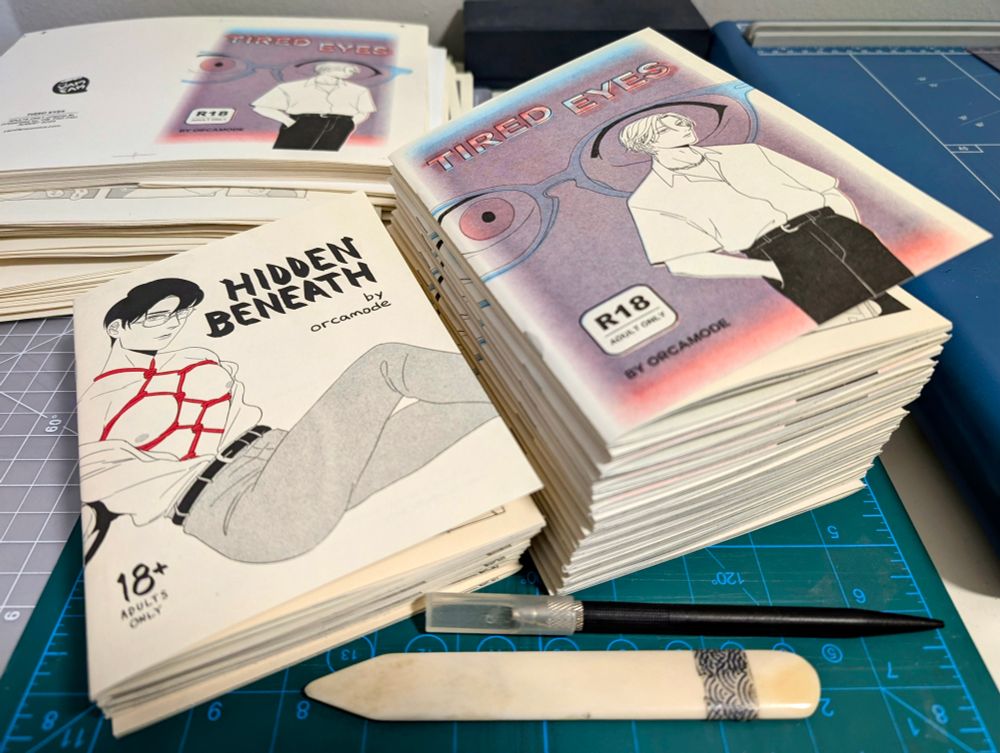 photo of two stacks of riso zines. one is titled Hidden Beneath and the other is Tired Eyes.