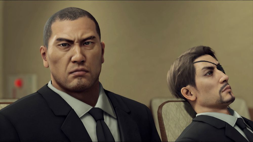 Majima and Saejima in dark suits, sitting beside each other, Saejima is upright and alert, Majima is slouching and staring off
