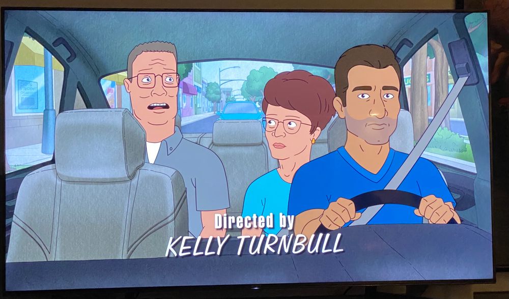 Screenshot from King of the Hill Season 14, Episode 01, Return of the King, Hank and Peggy sit in a car with a rideshare driver, Chyron reads “Directed By Kelly Turnbull”