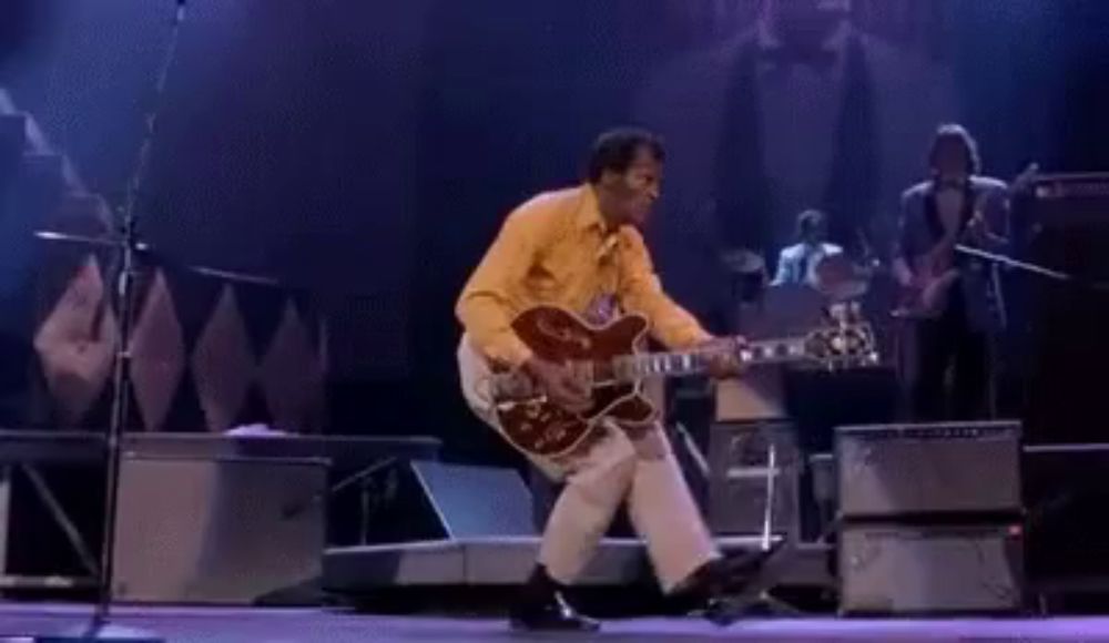 a man is playing a guitar on a stage while dancing .