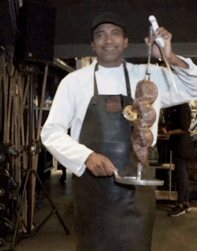 a man wearing an apron is holding a skewer of meat