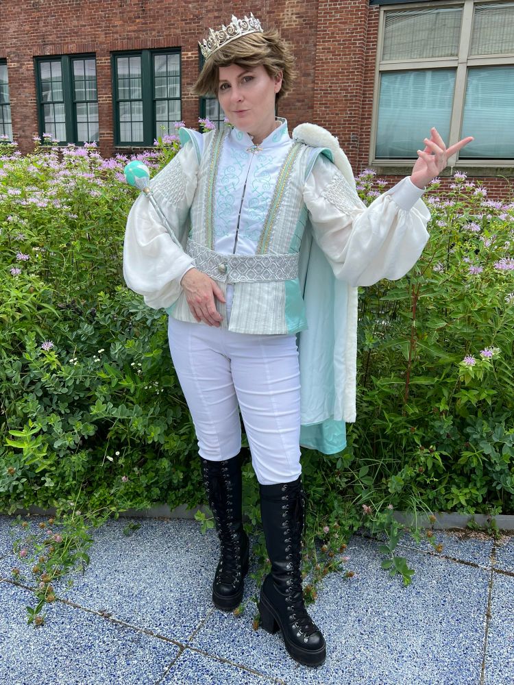 A cosplayer of Oikawa from Haikyuu, he has brown hair and a silver and white king outfit with a silver crown and a volleyball scepter.