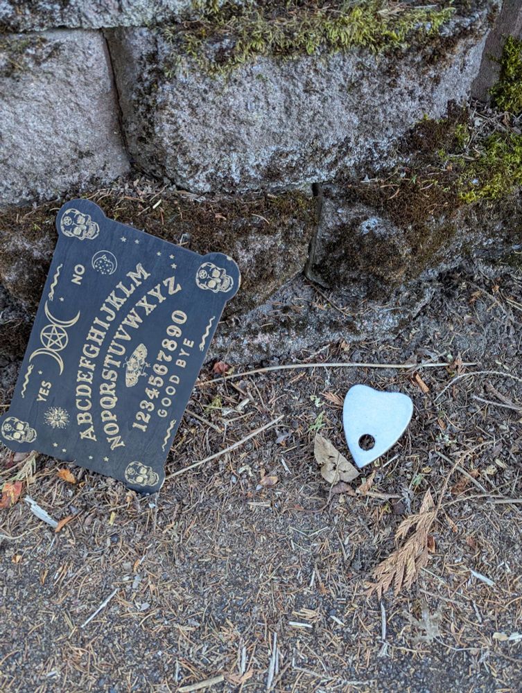 A Ouija board laying in the dirt against a rock wall.
