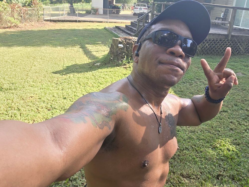 A shirtless Caleb flashes a peace sign in the middle of his freshly-mowed back yard