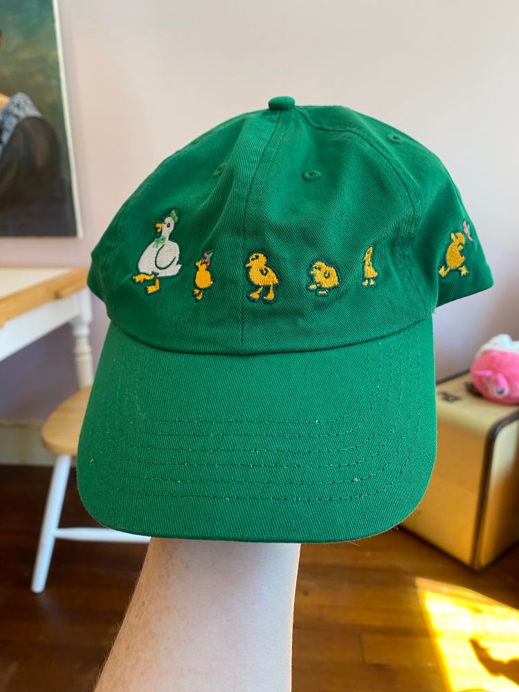 green hat with ducklings following in a line behind mom (artist: natali koromoto)