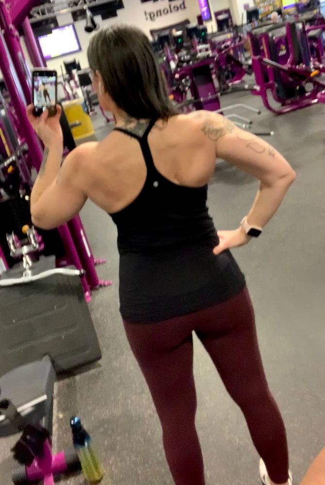 A woman taking a backside selfie wearing a black tank top and burgundy leggings 