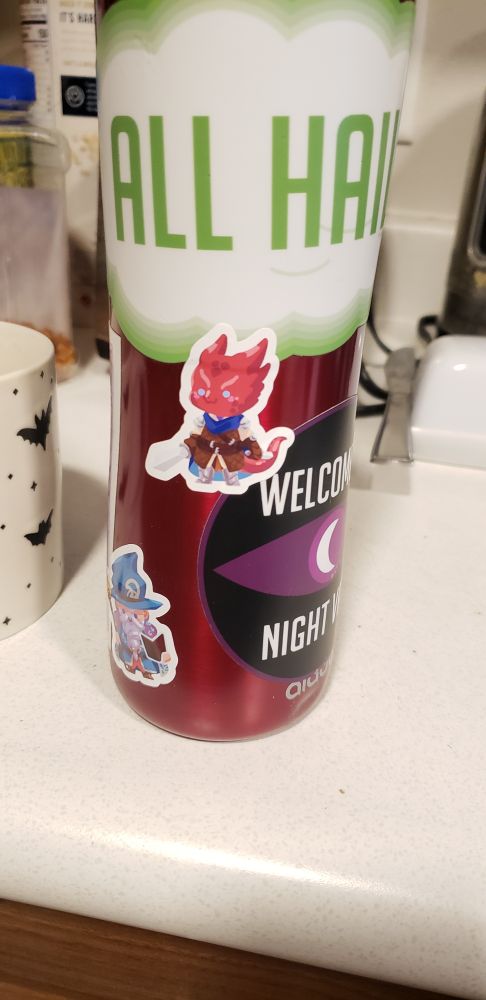A red thermos covered in stickers. Some of them are from the podcast Welcome to Nightvale and some are chibi adventurer characters done by Rozziesthebars