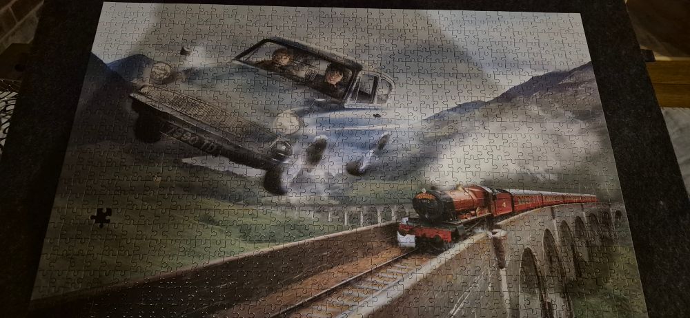 Image of a 1000 piece jigsaw of Harry Potter and Ron Weasley flying in a blue Ford Anglia above the Hogwarts Express 