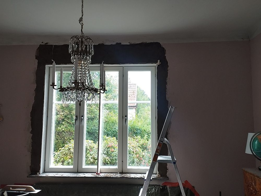 Ett rum med rosa väggar, en kristallkrona i taket och numera murad kant runt fönstret. 