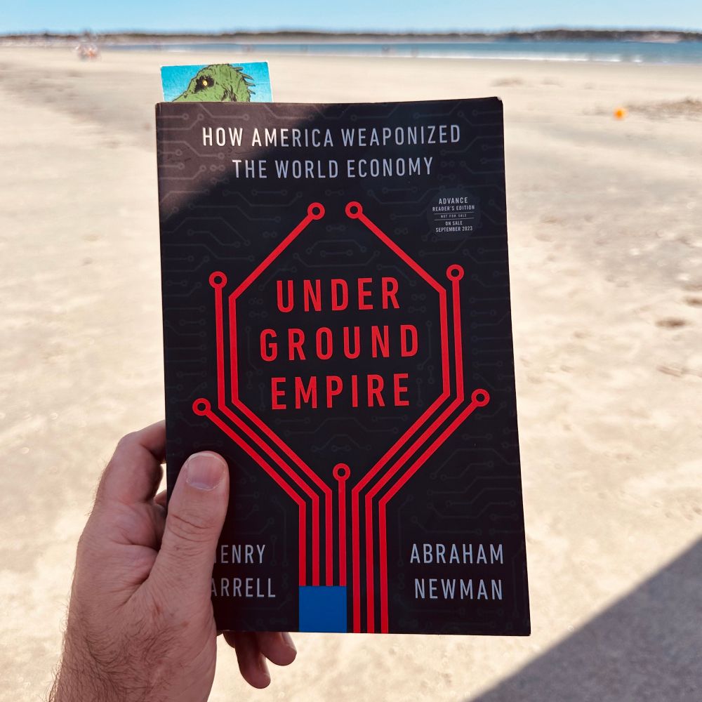 Picture of a hand holding a copy of the Underground Empire book with a beach background.