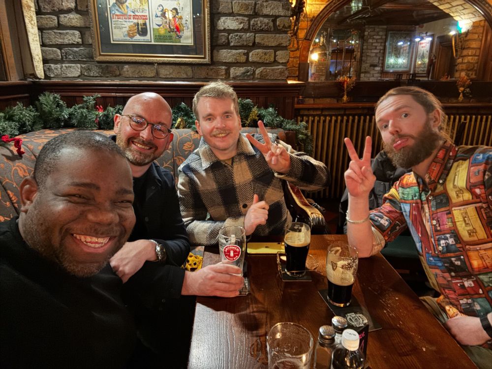 Four people in a pub in Ireland drinking pints of Guinness, one of them (Karl) is wearing a loud shirt and pulling a silly face and we don't know why.