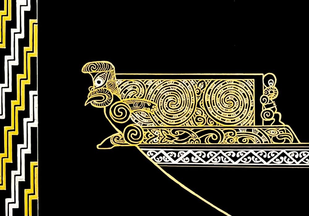 Close up of the ornately carved bow of the waka, in gold and silver on a black background.